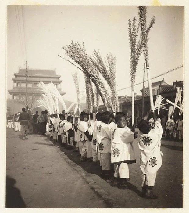 1933年，朝阳门内送殡队伍里手举纸扎雪柳的儿童列队道路两侧。